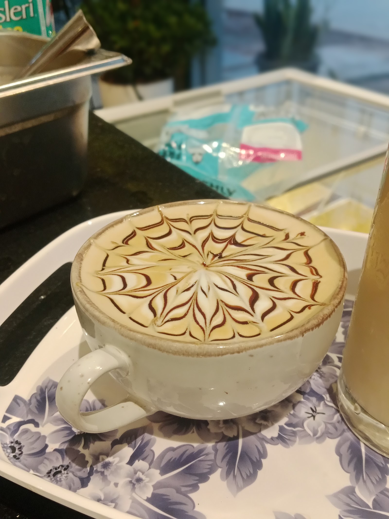 A cappuccino finished with a feathered chocolate rosette, on a saucer at the counter