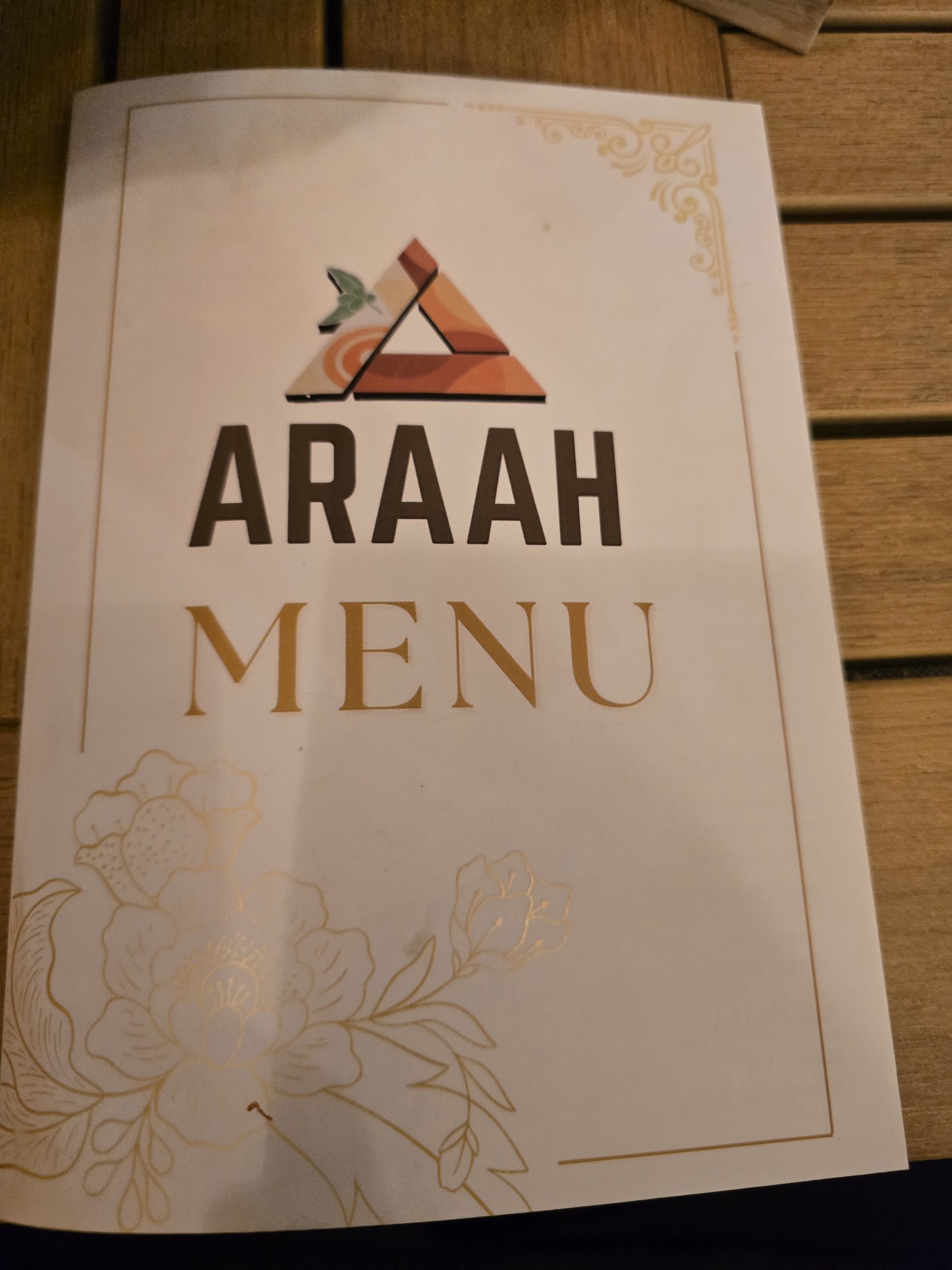 The cover of Araah's printed menu: the terracotta triangle logo with a green leaf, 'ARAAH' in heavy charcoal type and 'MENU' in gold