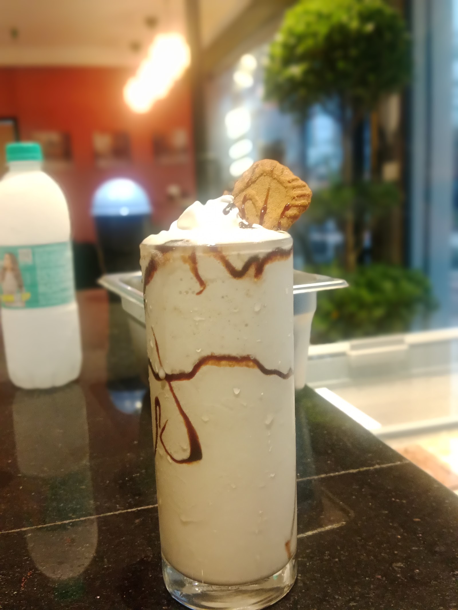 A tall Biscoff milkshake topped with whipped cream, caramel drizzle and a Biscoff biscuit, on the counter