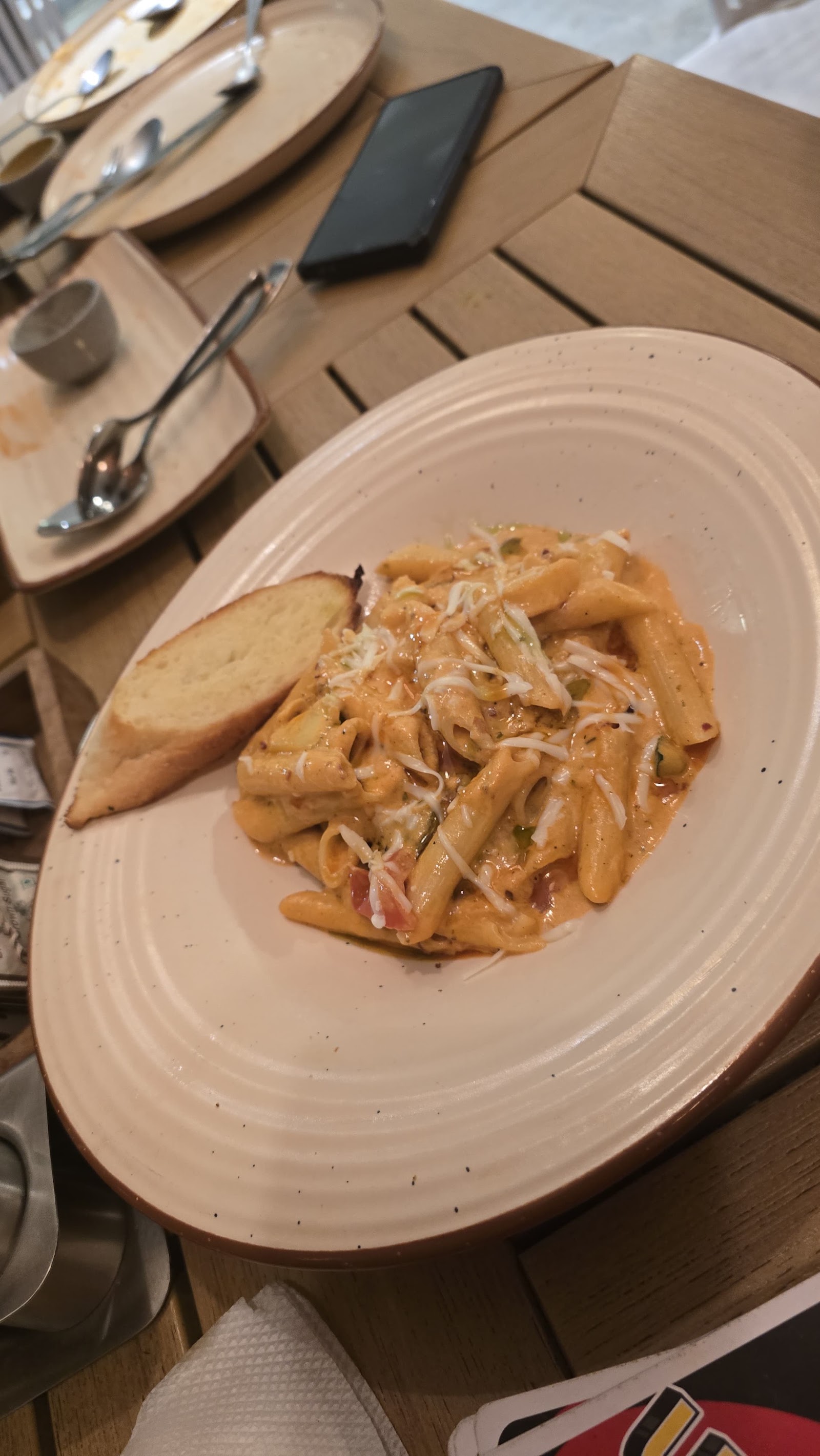 Penne in a creamy tomato sauce with garlic bread, on an oval plate at a wooden table