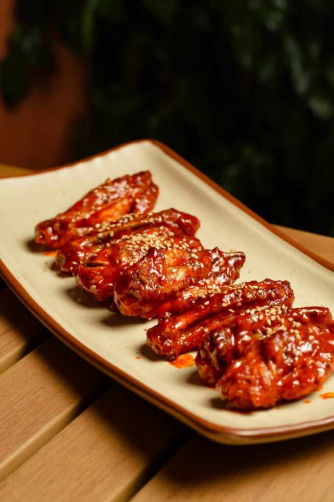 Peri peri chicken wings glazed dark and scattered with sesame seeds, on a cream plate at a wooden table