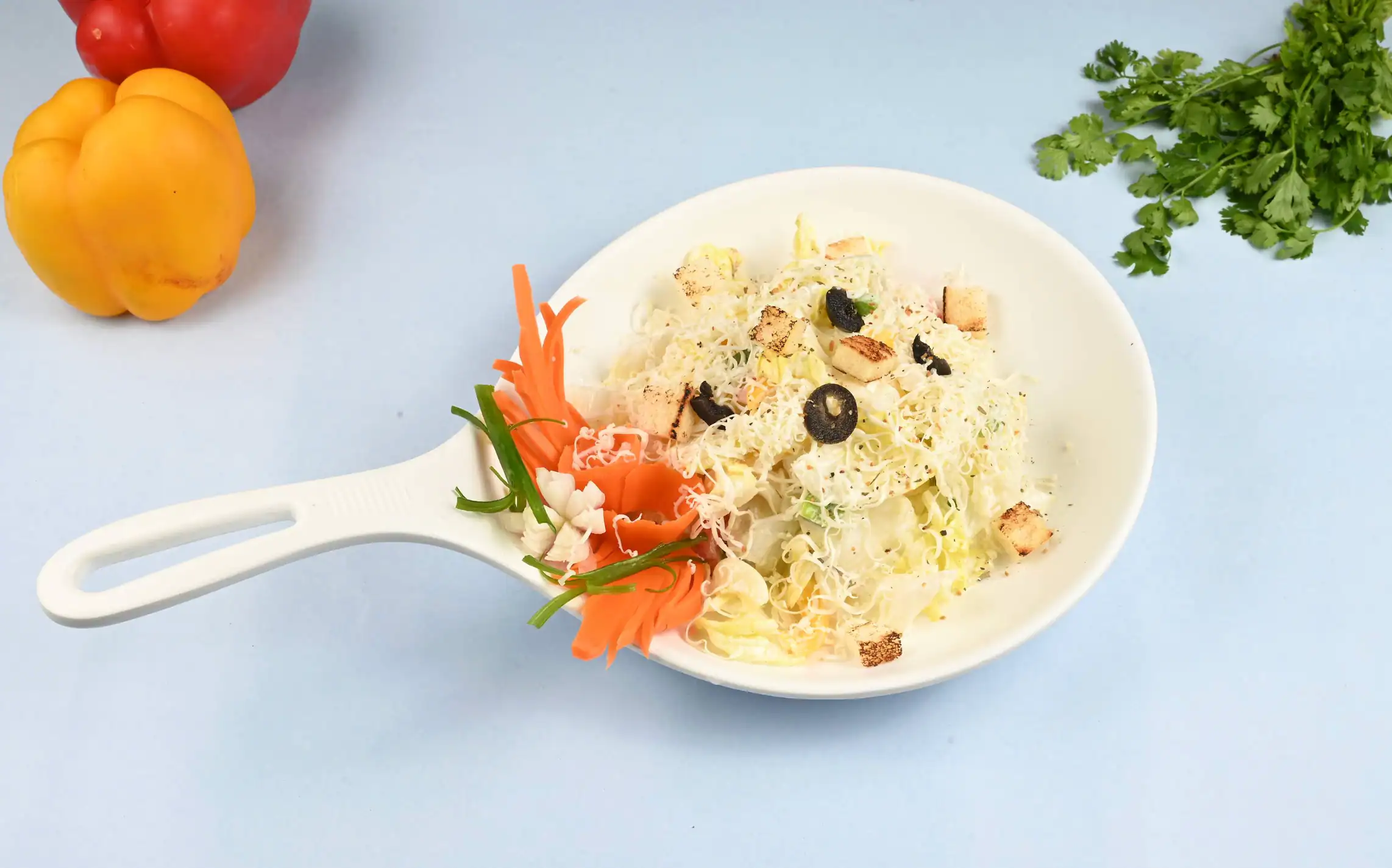 Caesar salad in a white pan-handled dish with croutons, olives and shaved cheese, on a pale blue surface