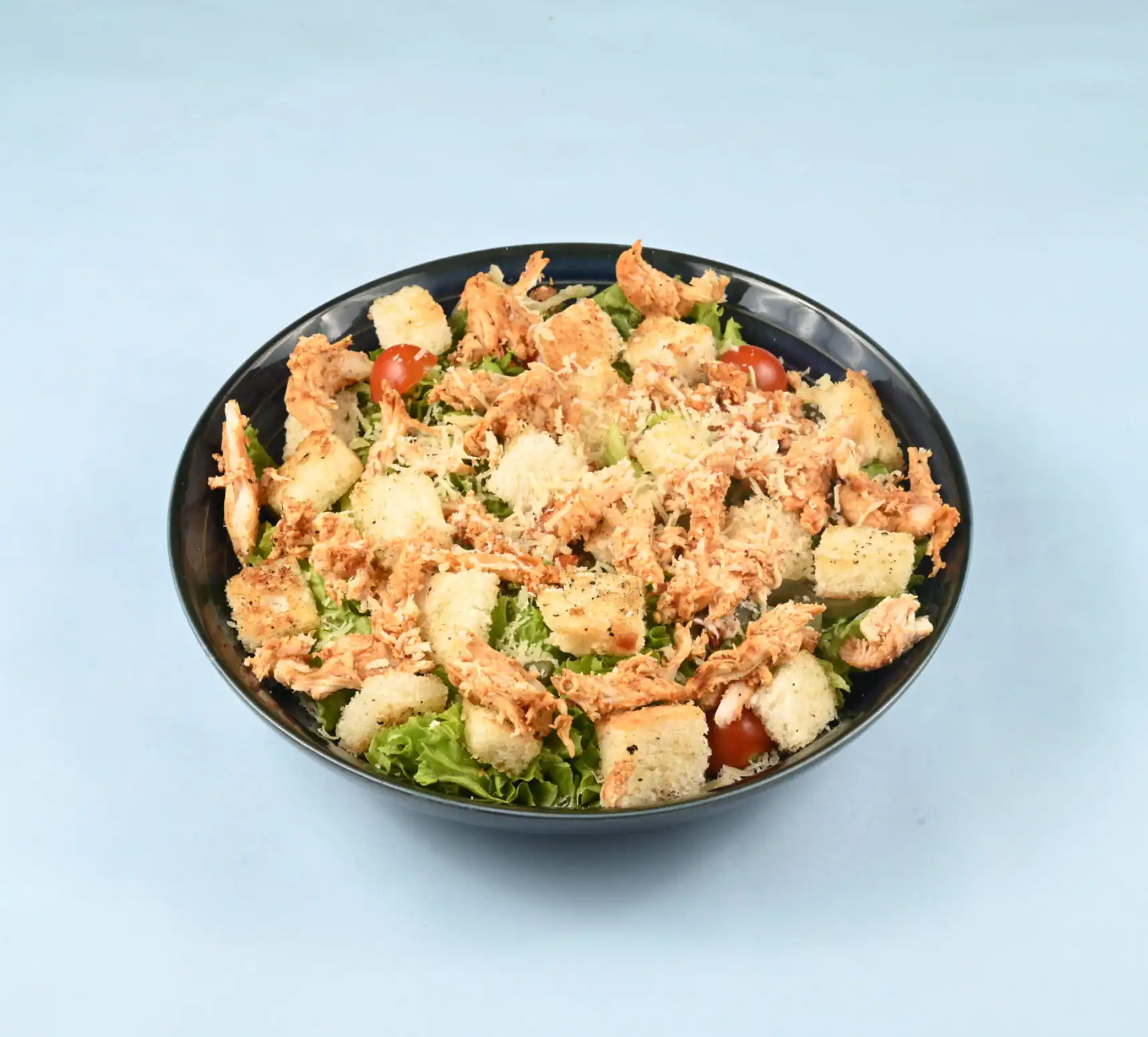 Caesar salad with chicken in a dark bowl, with croutons, cherry tomatoes and parmesan