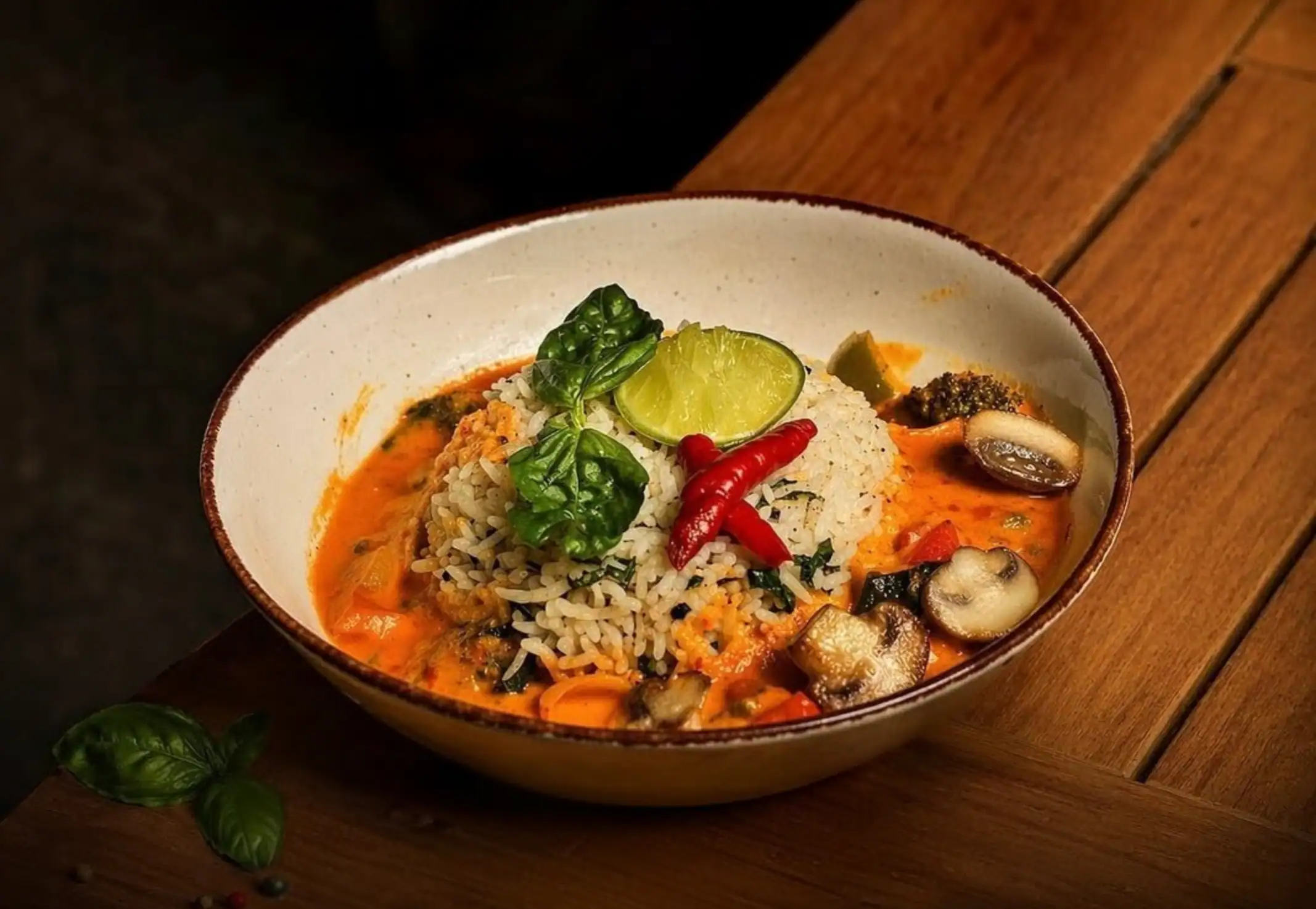 Thai green curry rice bowl — jasmine rice in a red coconut curry with basil, lime and chillies, on dark wood