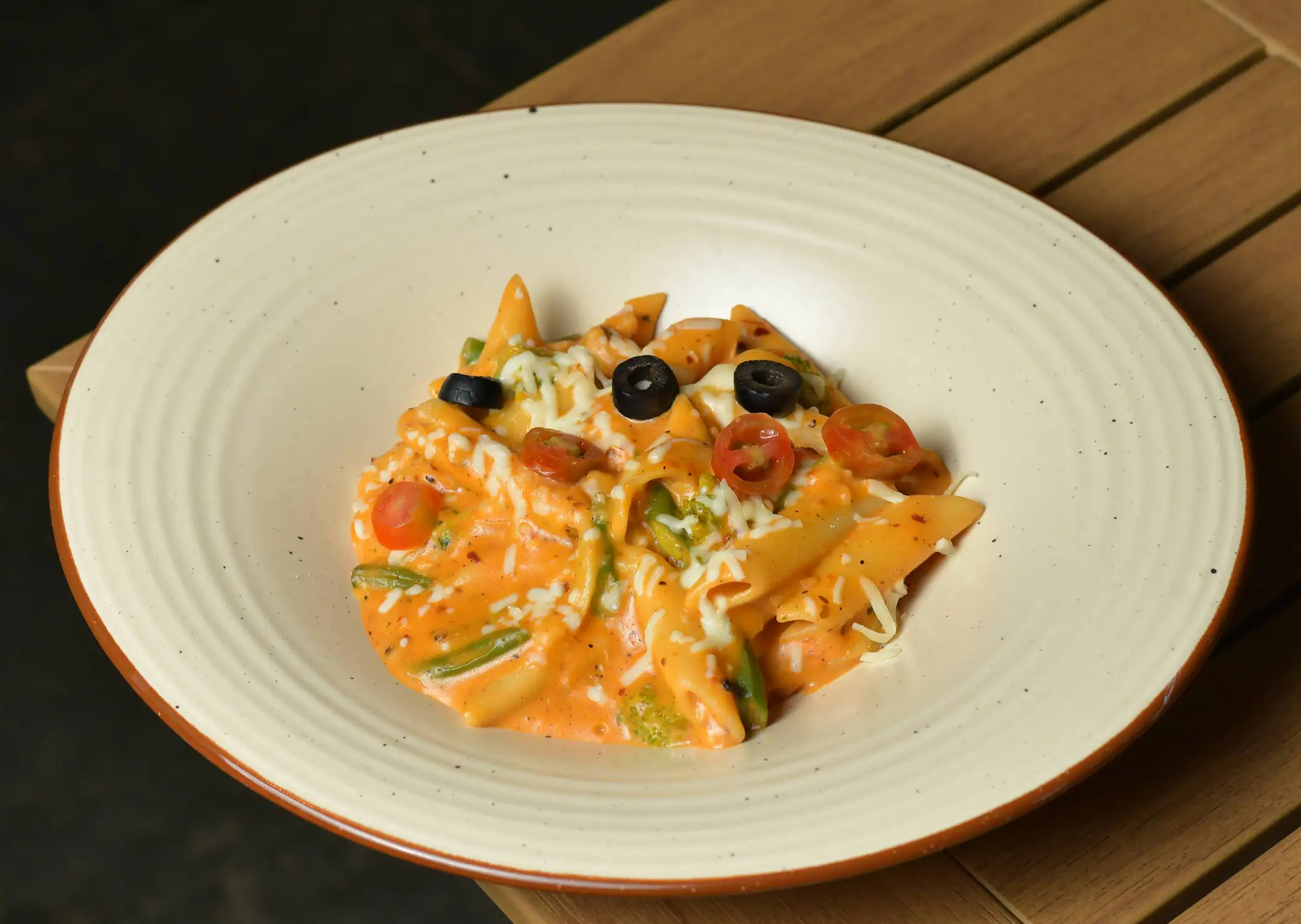 Arrabbiata penne in a speckled ceramic bowl, with olives, cherry tomatoes and melted cheese